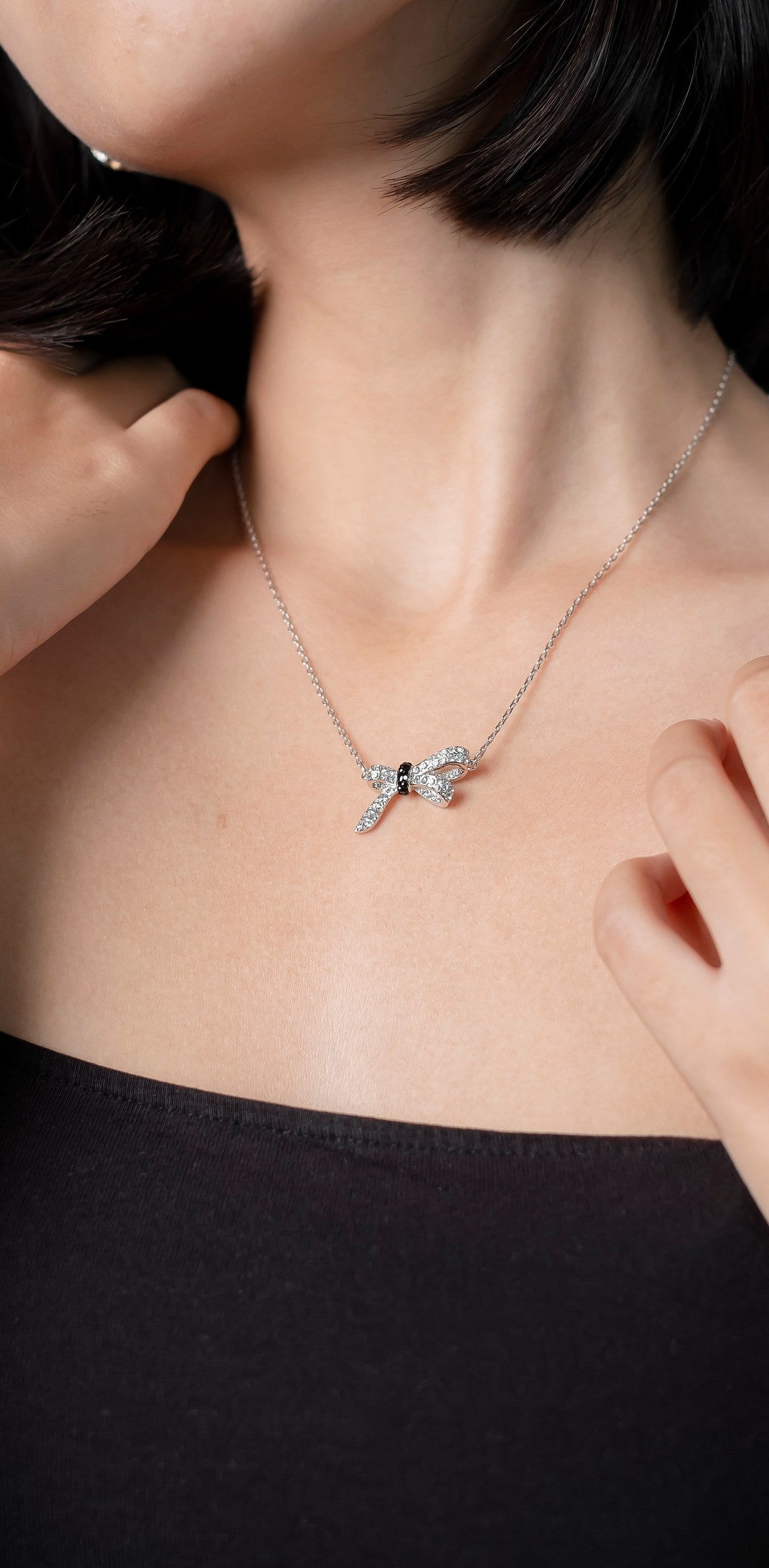 Woman wearing a fine silver chain necklace with a small pendant, against a black top