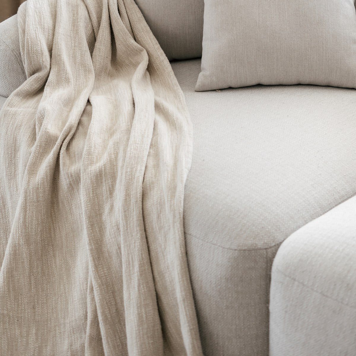 Cream woven throw blanket draped over a pale linen sofa in soft daylight