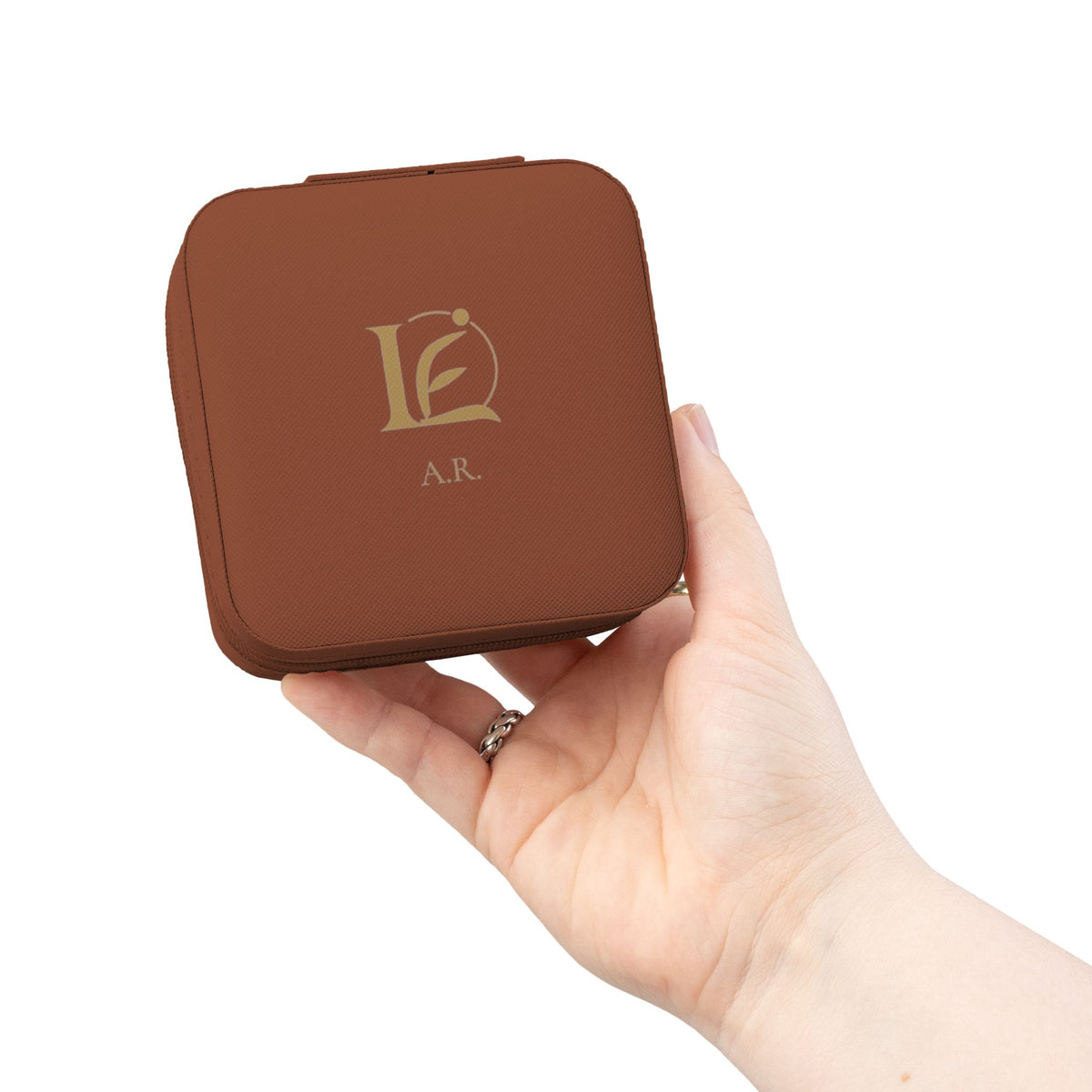 The Keepsake Travel Case in cognac brown, held in hand, with gold Lyfe Element mark and initials